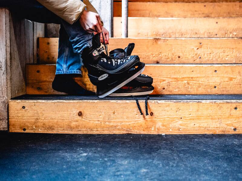Eine Person sitzt auf einer Holztreppe und bindet ihre schwarzen Schlittschuhe.