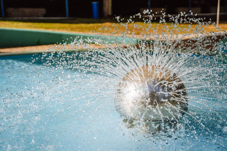 Eine silberne Kugel erzeugt in einer Wasserskulptur kreisförmig sprühende Wasserstrahlen in einem klaren Wasserbecken.